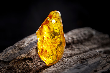 Image showing Natural amber. A piece of yellow transparent natural amber on large piece of dark stoned wood.