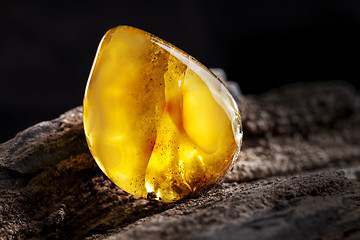 Image showing Natural amber. A piece of yellow opaque natural amber on large piece of dark stoned wood.