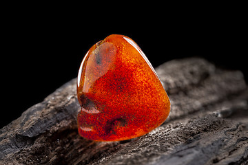 Image showing Natural amber. A piece of yellow and red semi transparent natural amber on piece of stoned wood.