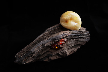 Image showing Natural amber. A piece of yellow opaque natural amber on large piece of dark stoned wood.