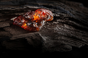 Image showing Natural amber. A piece of yellow and red semi transparent natural amber on piece of stoned wood.