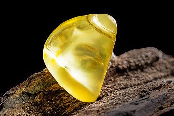 Image showing Natural amber. A piece of yellow opaque natural amber on large piece of dark stoned wood.