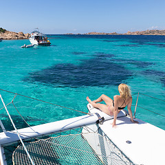 Image showing Woman relaxing on a summer sailing cruise, sitting on a luxury catamaran near picture perfect white sandy beach on Spargi island in Maddalena Archipelago, Sardinia, Italy.