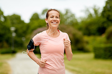 Image showing woman with earphones add armband jogging at park