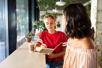 Image showing woman with friend at cafe writing to notebook