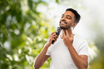 Image showing smiling indian man shaving beard with trimmer