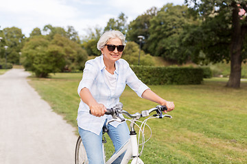 Image showing happy senior woman riding bicycle at summer park