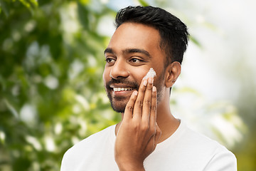 Image showing man applying cream to face over natural background