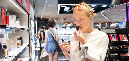 Image showing Beautiful blond young woman choosing perfume in retail store. Lady testing and buying cosmetics in beauty store