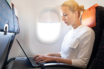 Image showing Attractive caucasian female passenger working at modern laptop computer using wireless connection on board of commercial airplane flight