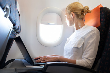 Image showing Attractive caucasian female passenger looking through the plain window while working on modern laptop computer using wireless connection on board of commercial airplane flight