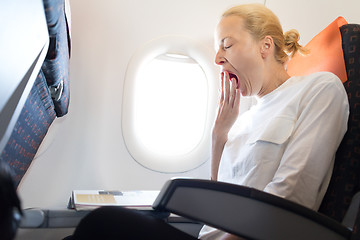 Image showing Beautiful casual caucasian woman yawning on airplane flight while reading in flight magazine.