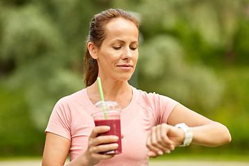 Image showing woman with smoothie looking at smart watch in park