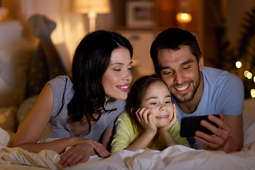 Image showing happy family with smartphone in bed at night