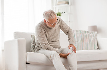 Image showing senior man suffering from knee ache at home