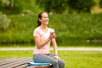 Image showing woman drinking smoothie after exercising in park