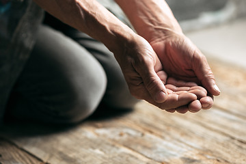 Image showing Male beggar hands seeking money on the wooden floor at public path way