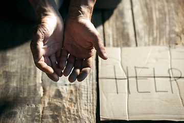 Image showing Male beggar hands seeking money on the wooden floor at public path way