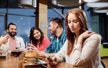 Image showing bored woman messaging on smartphone at restaurant