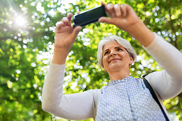 Image showing senior woman photographing by cell at summer park