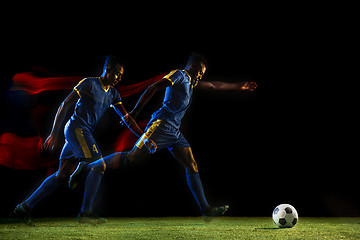 Image showing Male soccer player kicking ball on dark background in mixed light