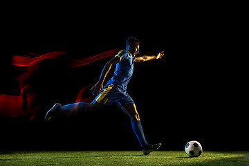 Image showing Male soccer player kicking ball on dark background in mixed light