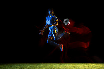 Image showing Male soccer player kicking ball on dark background in mixed light