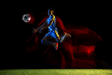 Image showing Male soccer player kicking ball on dark background in mixed light
