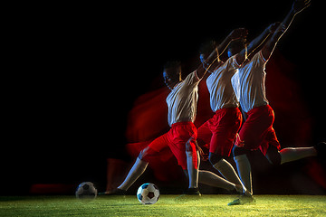 Image showing Male soccer player kicking ball on dark background in mixed light