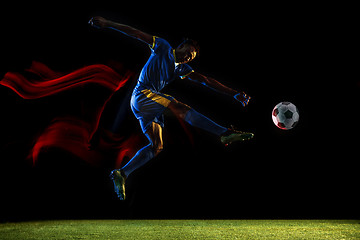 Image showing Male soccer player kicking ball on dark background in mixed light