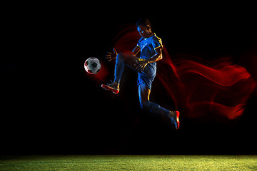 Image showing Male soccer player kicking ball on dark background in mixed light