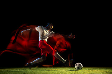 Image showing Male soccer player kicking ball on dark background in mixed light