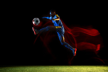 Image showing Male soccer player kicking ball on dark background in mixed light