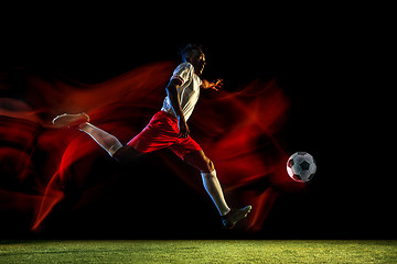 Image showing Male soccer player kicking ball on dark background in mixed light