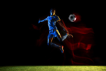 Image showing Male soccer player kicking ball on dark background in mixed light