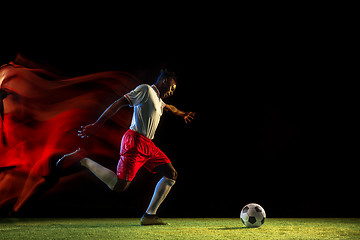 Image showing Male soccer player kicking ball on dark background in mixed light