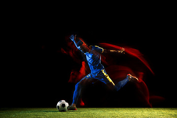 Image showing Male soccer player kicking ball on dark background in mixed light