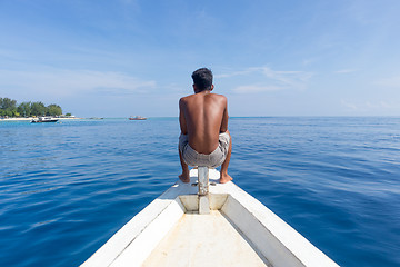 Image showing Local Sporty Guy Sitting Topless at the Bow of Traditional White Wooden Sail Boat, Looking At Beautiful Blue Sea of Gili Islands near Bali, Indonesia