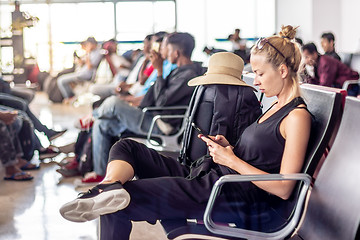 Image showing Female traveler talking on cell phone while waiting to board a plane at departure gates at asian airport terminal.