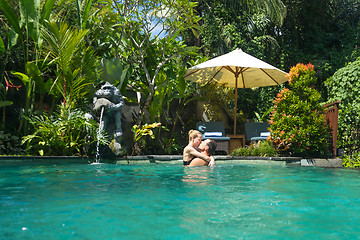 Image showing Happy couple kissing while relaxing in outdoor spa infinity swimming pool surrounded with lush tropical greenery of Ubud, Bali. Luxury spa and wellness vacation retreat concept