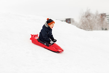 Image showing happy boy sliding on sled down snow hill in winter