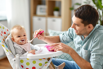 Image showing father feeding happy baby in highchair at home