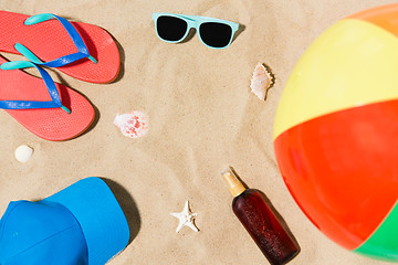 Image showing cap, flip flops and shades and beach ball on sand