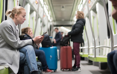 Image showing Beautiful blonde woman wearing winter coat reading on the phone while traveling by metro public transport.