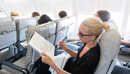 Image showing Woman reading magazine on airplane during flight. Female traveler reading seated in passanger cabin.