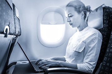 Image showing Attractive caucasian female passenger working at modern laptop computer using wireless connection on board of commercial airplane flight