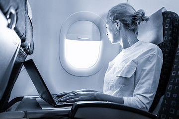 Image showing Attractive caucasian female passenger looking through the plain window while working on modern laptop computer using wireless connection on board of commercial airplane flight