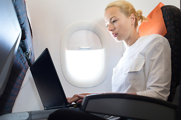 Image showing Attractive caucasian female passenger working at modern laptop computer using wireless connection on board of commercial airplane flight