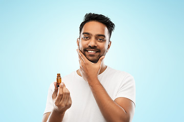 Image showing smiling indian man applying grooming oil to beard