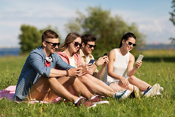 Image showing smiling friends with smartphones sitting on grass